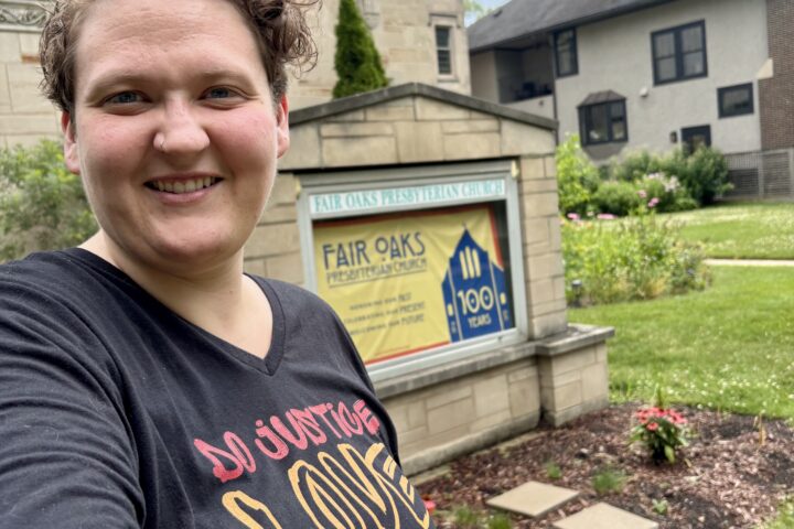 Kori, in a black shirt, standing in front of a sign that says Fair Oaks Presbyterian Church on it.