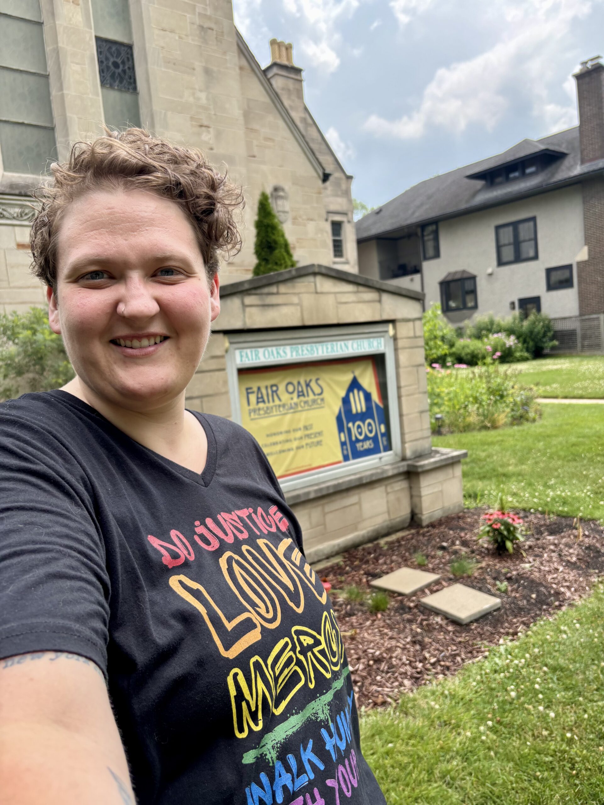 Kori, in a black shirt, standing in front of a sign that says Fair Oaks Presbyterian Church on it.